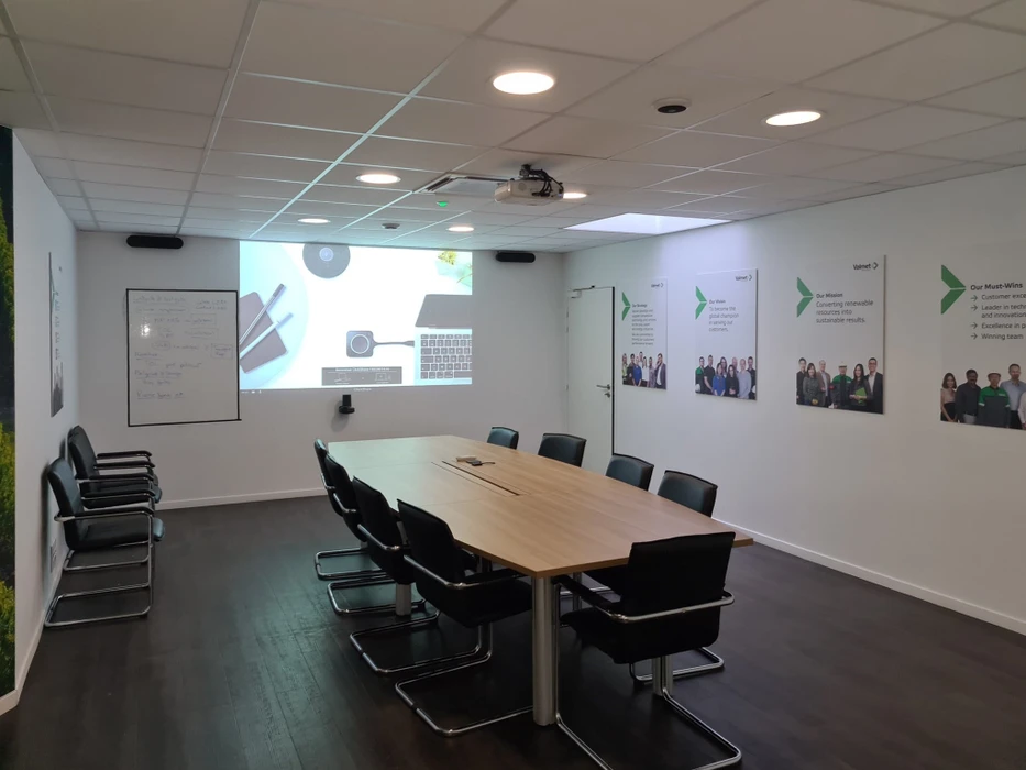 Salle de conférence avec audience assise écoutant un présentateur debout devant un écran de projection blanc