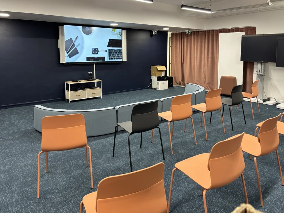 Salle de conférence avec audience assise écoutant un présentateur debout devant un écran de projection