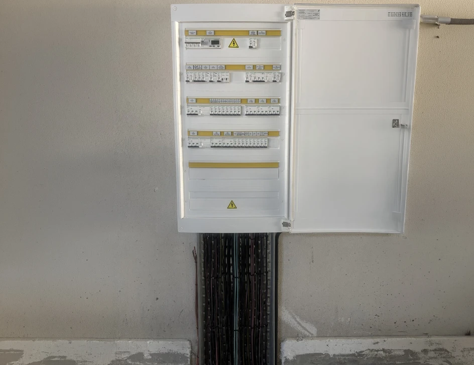 Technicien électricien en intervention extérieure utilisant un multimètre pour diagnostiquer un tableau électrique ouvert