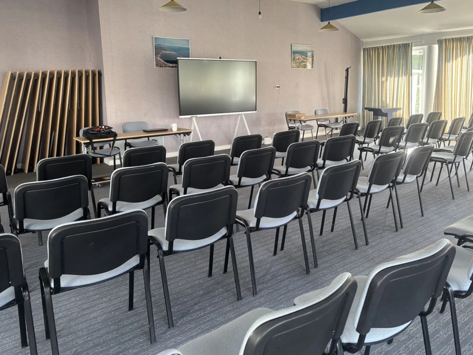 Photographie professionnelle d'une salle de conférence haut de gamme avec installations audiovisuelles intégrées : grands écrans muraux incurvés, système de visioconférence de qualité professionnelle avec caméras motorisées, tableau blanc interactif, système d'éclairage ambiant ajustable, panneaux acoustiques modernes, mobilier premium, et câblage dissimulé. La salle doit montrer l'intégration seamless des technologies avec une atmosphère professionnelle et sophistiquée.